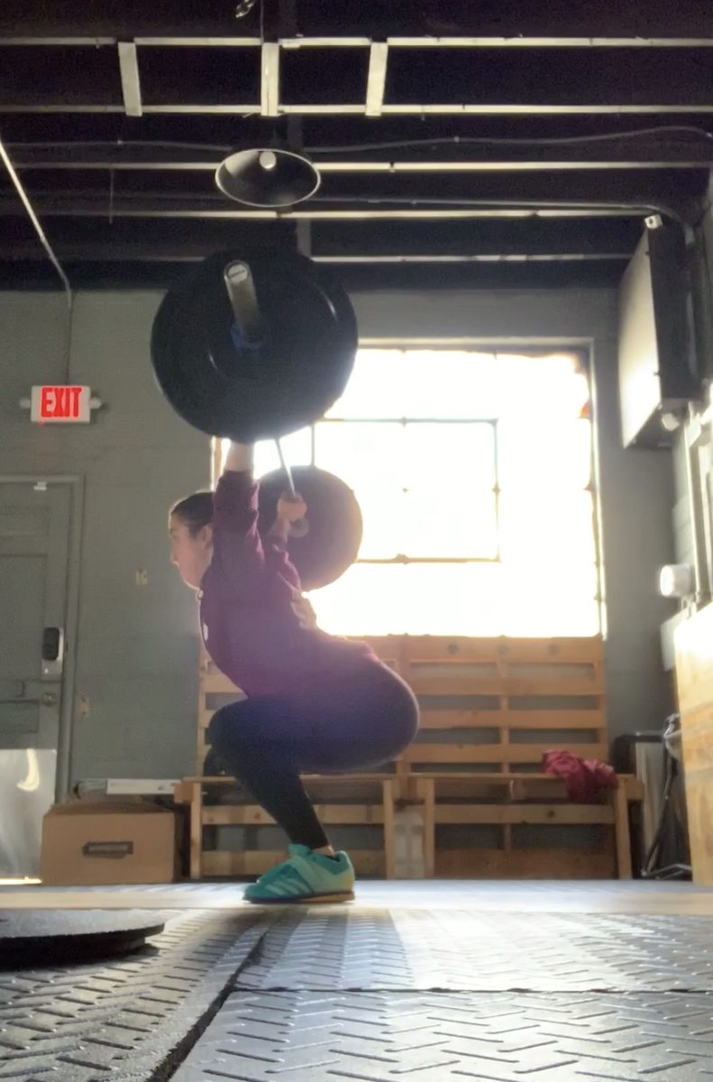 Jess catching a loaded barbell overhead in a squat inside a garage gym